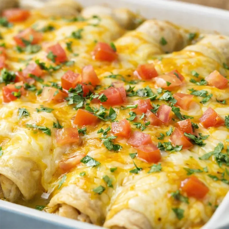 Baked chicken enchiladas in a dish topped with melted cheese, diced tomatoes and cilantro