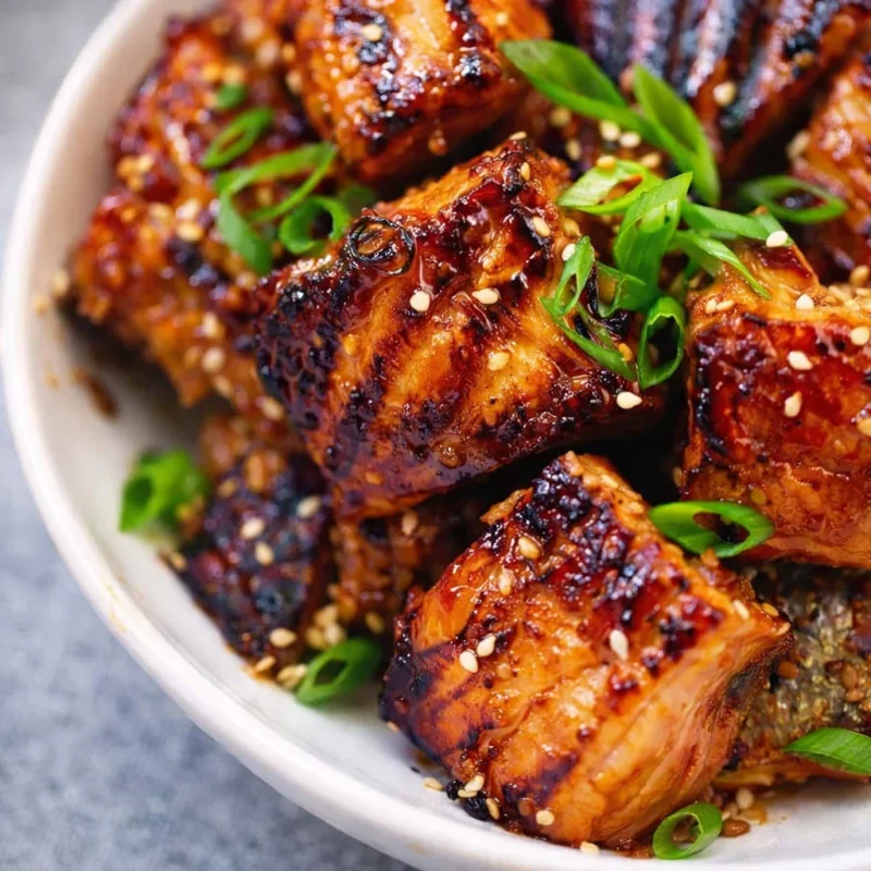 Honey garlic salmon bites glazed with sauce and topped with green onions and sesame seeds