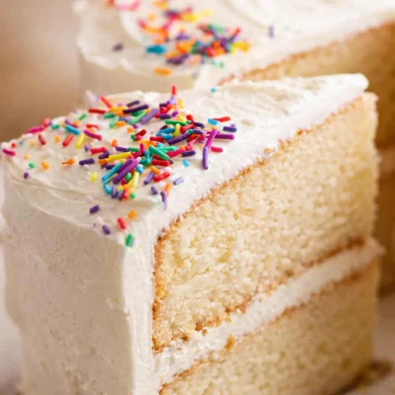 Slice of layered vanilla cake with vanilla buttercream and rainbow sprinkles, made from this simple vanilla cake recipe