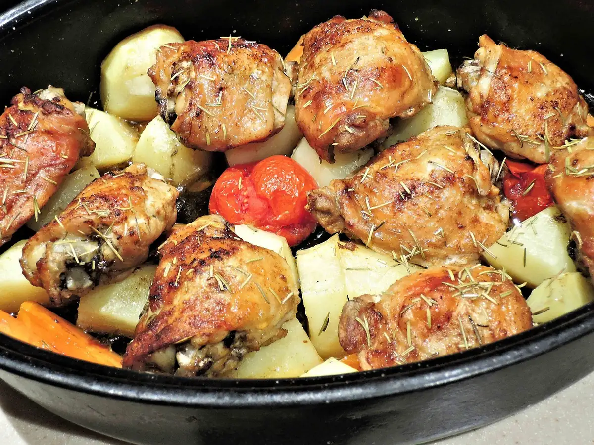 Oven roasted chicken thighs with potatoes and tomatoes in a dark roasting pan