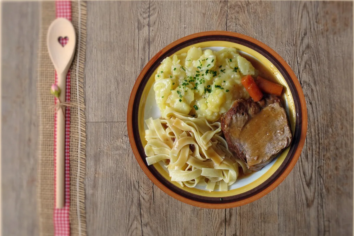 Plate of pot roast with carrots, buttered egg noodles and mashed potatoes