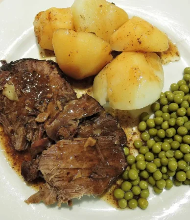 Crock pot chuck roast sliced and served with gravy, boiled potatoes and green peas