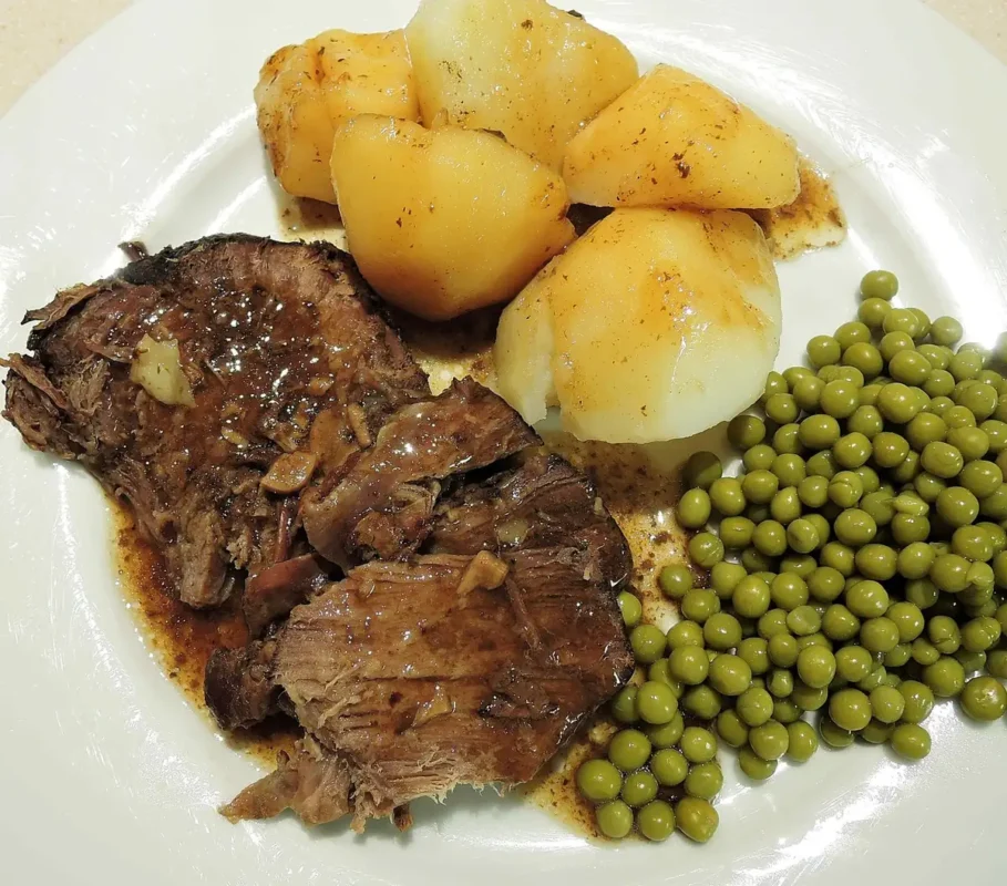 Crock pot chuck roast sliced and served with gravy, boiled potatoes and green peas