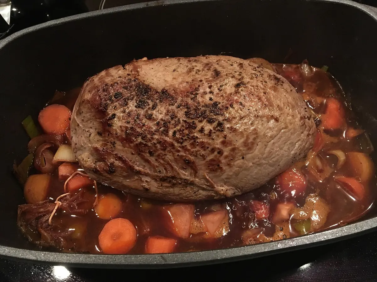 Browned beef chuck roast braising with carrots and onions in a pot