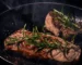 Two steaks seared in a cast-iron skillet with rosemary, the same pan method used for Denver steak