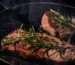 Two steaks seared in a cast-iron skillet with rosemary, the same pan method used for Denver steak