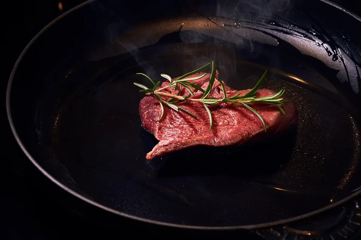 Raw beef steak with rosemary going into a hot cast-iron pan