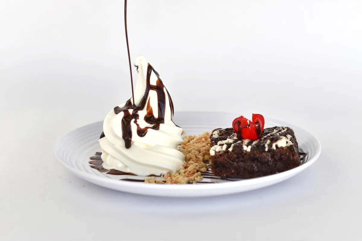 Chocolate dessert square topped with cherries, served with whipped cream and chocolate sauce