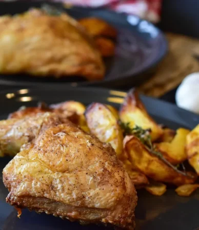 Golden chicken thigh with crisp skin and potato wedges, the result to aim for with this chicken thigh air fryer recipe