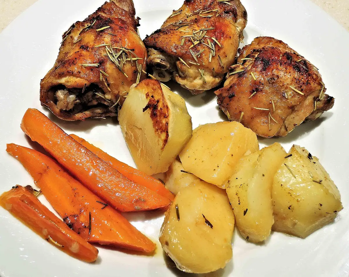 Herb-roasted chicken thighs served with potatoes and carrots on a white plate