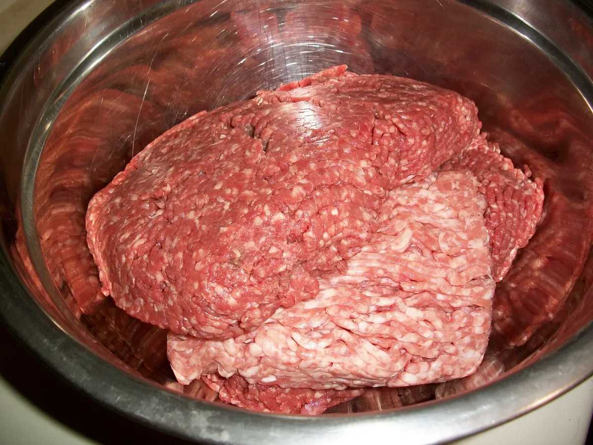 Block of raw ground beef in a stainless steel mixing bowl