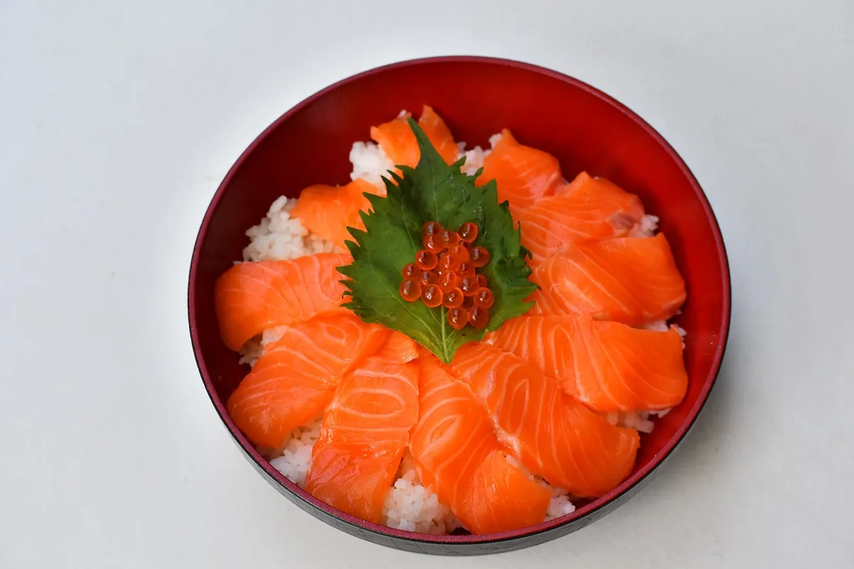 Bowl of rice topped with raw salmon slices, a shiso leaf and salmon roe