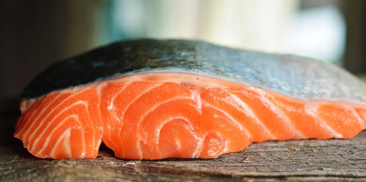 Fresh raw salmon fillet with bright orange flesh and silver skin on a wooden board