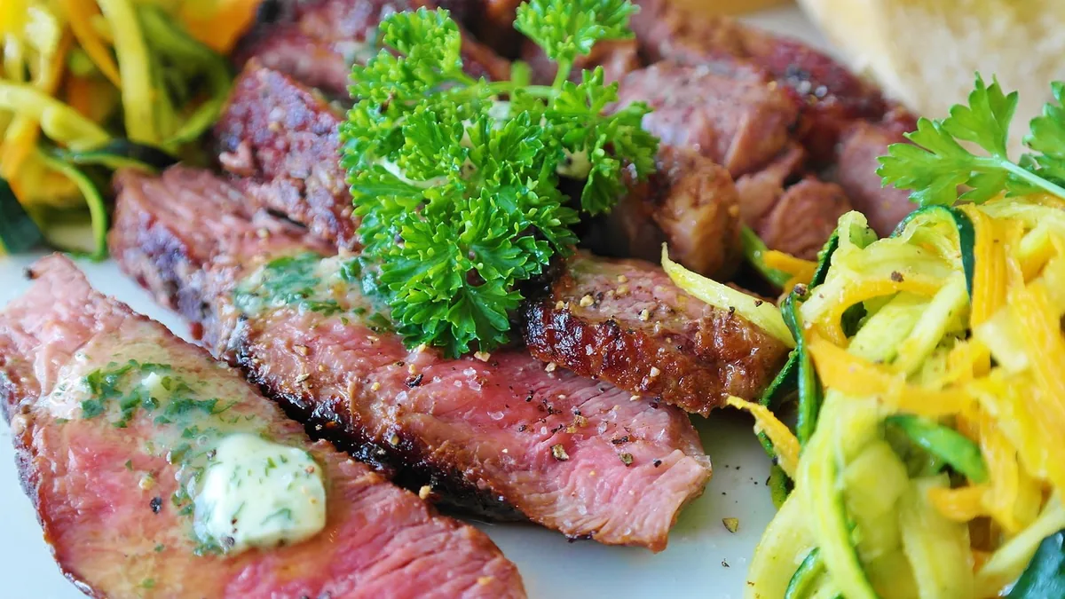 Sliced medium-rare steak topped with melting herb butter and parsley