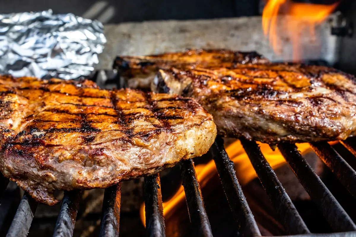 Steaks searing over high heat on a grill with flames below the grates