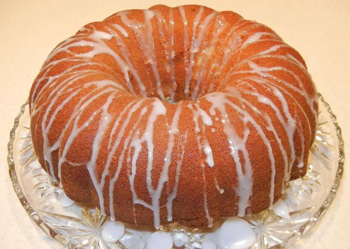 Golden bundt cake drizzled with white lemon glaze on a glass cake stand, just like a finished 7 Up pound cake