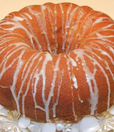 Golden bundt cake drizzled with white lemon glaze on a glass cake stand, just like a finished 7 Up pound cake