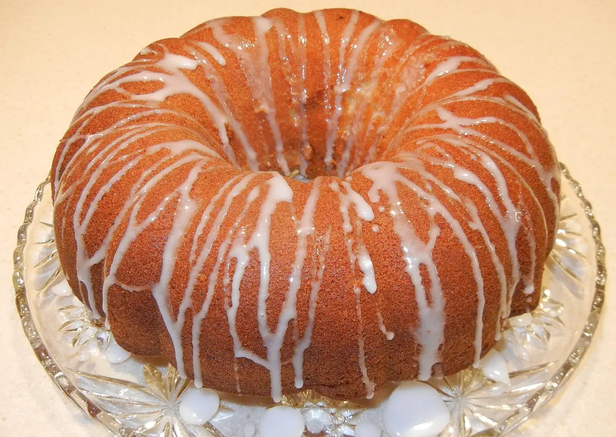 Golden bundt cake drizzled with white lemon glaze on a glass cake stand, just like a finished 7 Up pound cake
