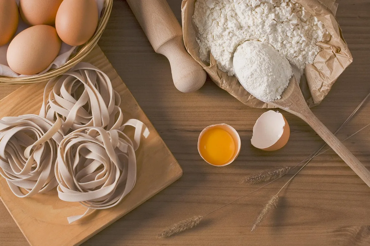 Nests of egg noodles on a wooden board with flour and eggs