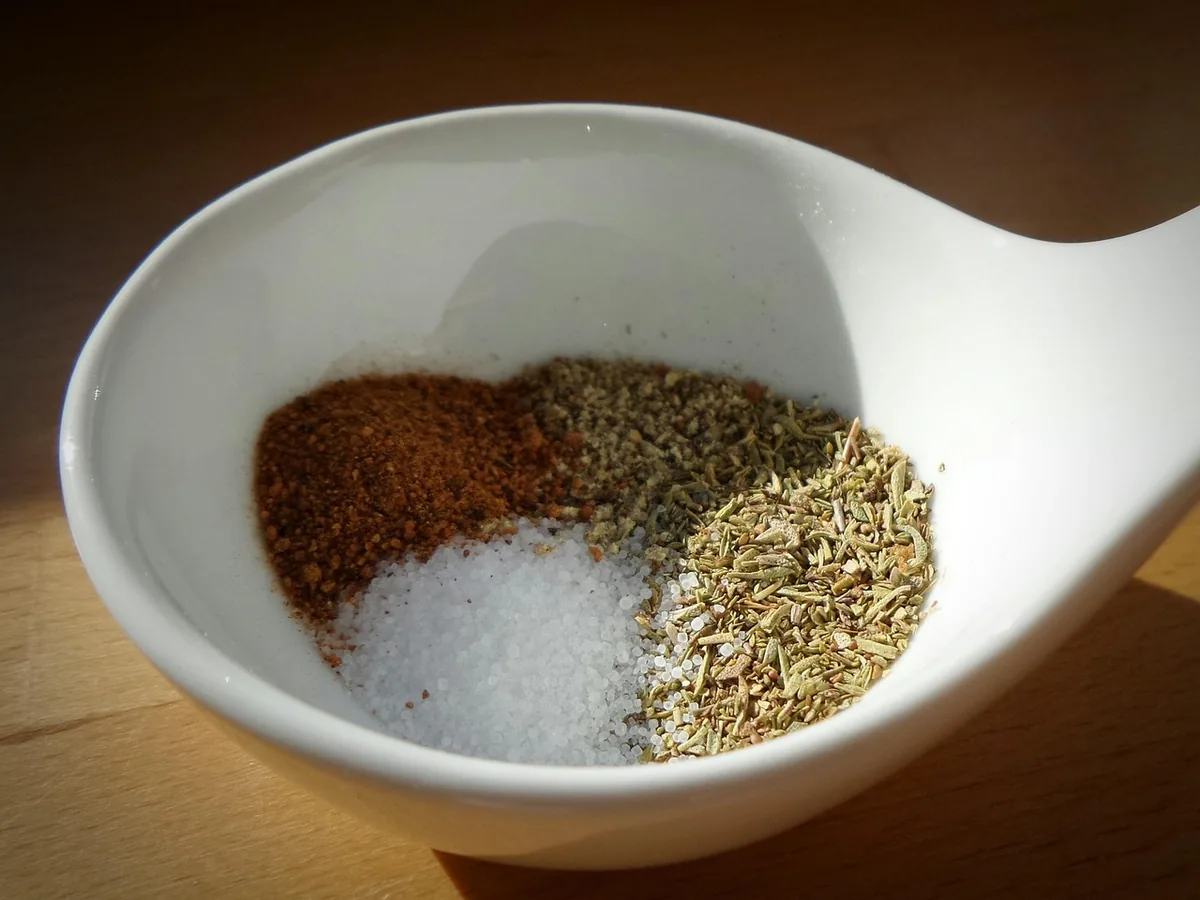 Small white bowl with paprika, salt and dried herbs ready to be stirred into a spice blend