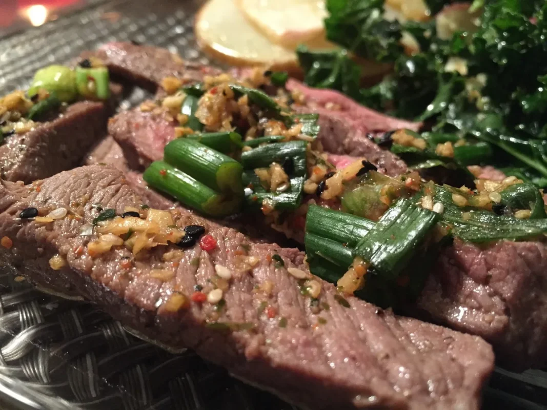 Sliced seared steak topped with garlic and green onions, like the result of this flat iron steak recipe