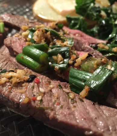 Sliced seared steak topped with garlic and green onions, like the result of this flat iron steak recipe