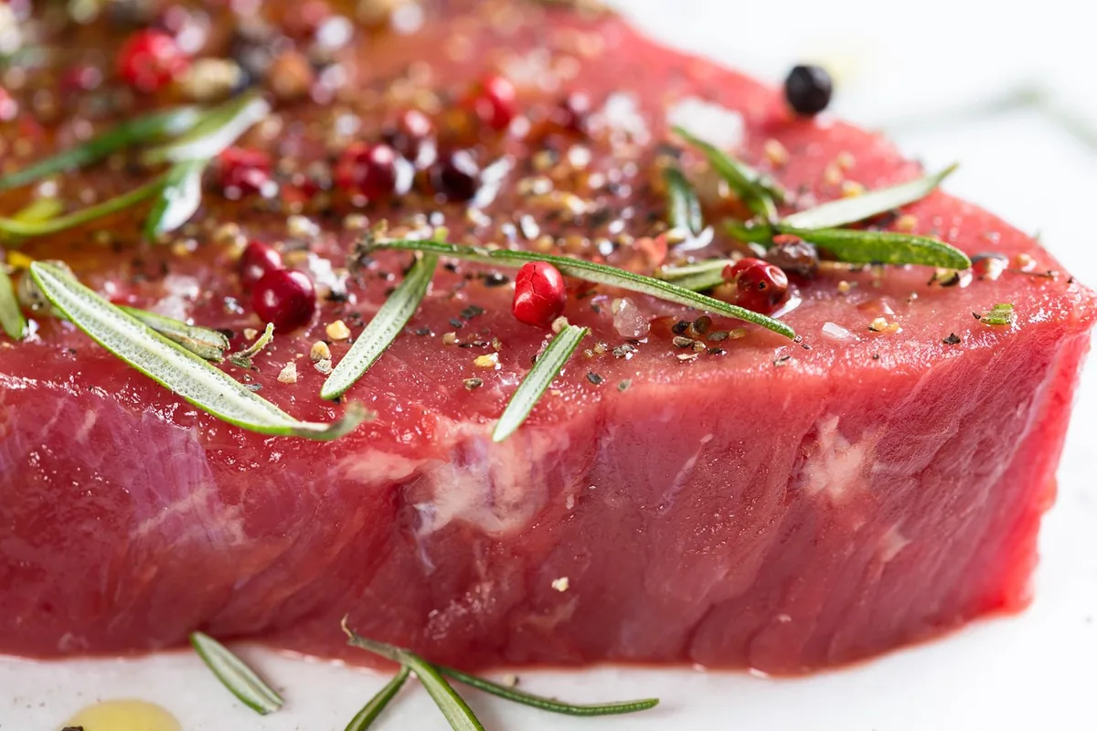 Raw beef steak seasoned with rosemary and peppercorns, ready to cook