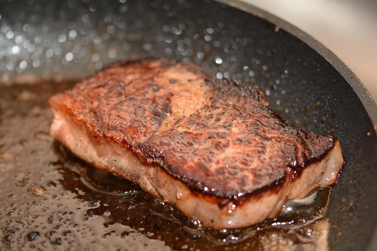 Steak searing in a hot skillet with a deep brown crust