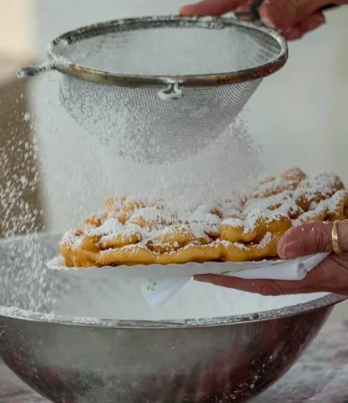 Powdered sugar being sifted over a fresh funnel cake, the finish for this funnel cake recipe