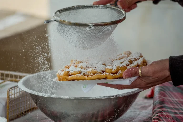 Powdered sugar being sifted over a fresh funnel cake, the finish for this funnel cake recipe