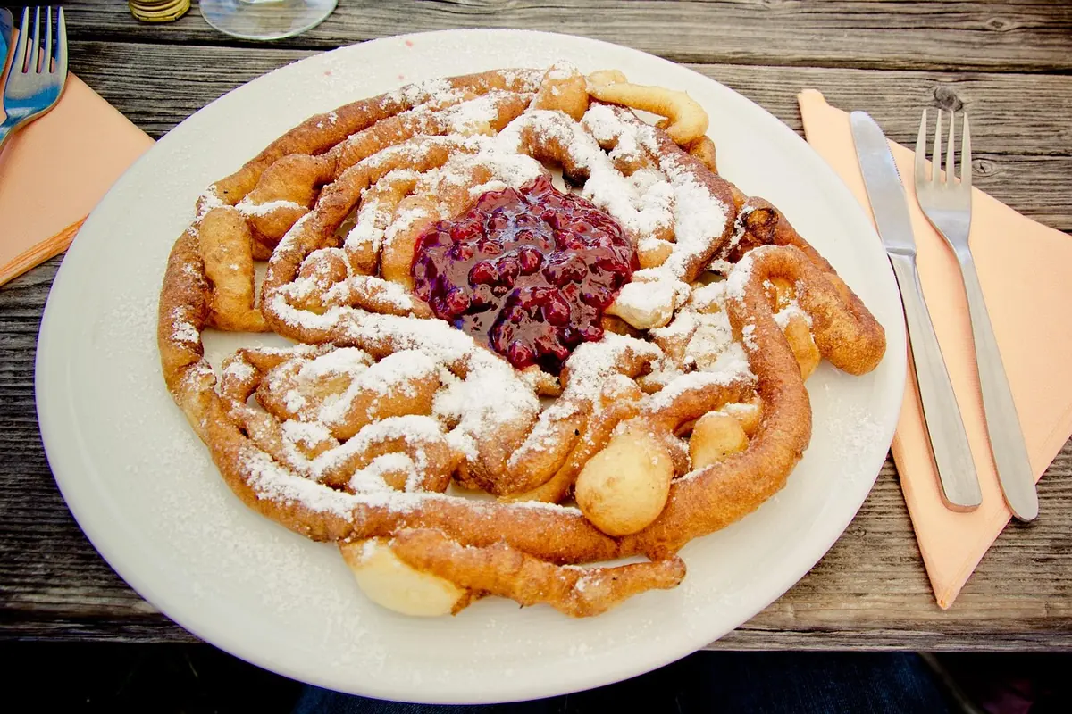 Funnel cake dusted with powdered sugar and topped with berry jam on a white plate
