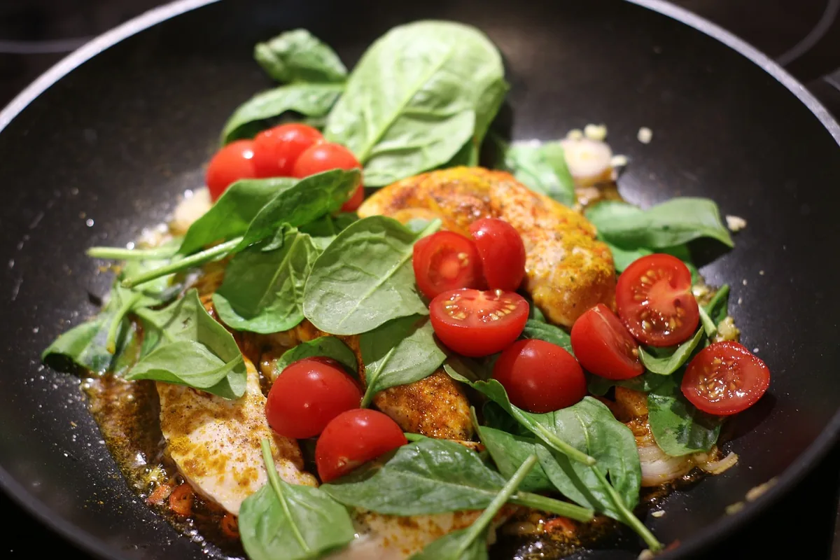 Seared chicken breast in a skillet topped with spinach and cherry tomatoes