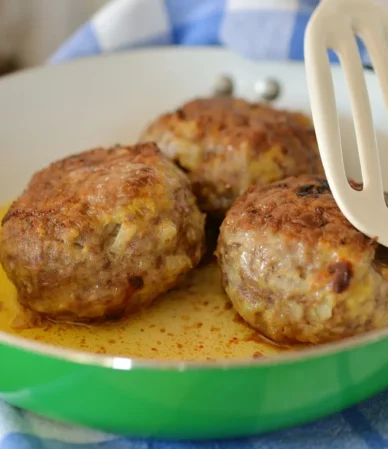 Browned meatballs in a green skillet with a spatula, like these gluten free meatballs