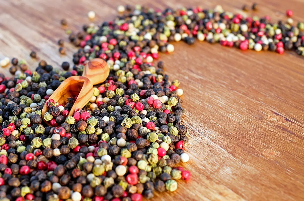 Mixed black, white, green and pink peppercorns on a wooden table with a wooden scoop
