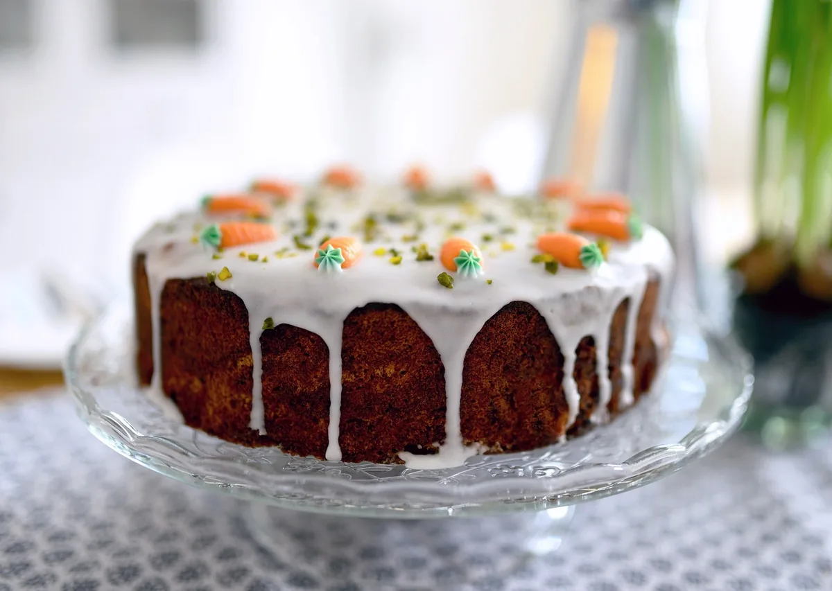 Whole carrot cake with white icing drizzled down the sides and small decorative carrots on top