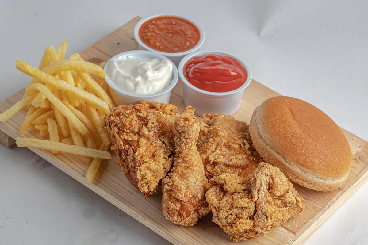 Fried chicken pieces with fries, a bun and dipping sauces on a wooden board
