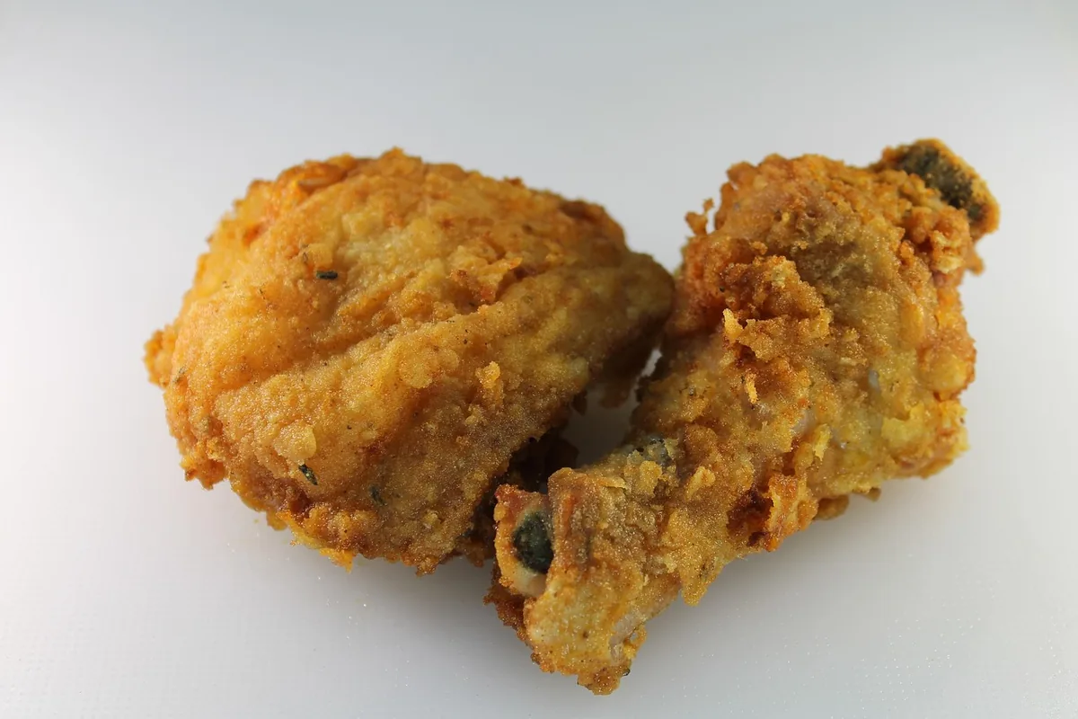 Two pieces of golden fried chicken with a crisp, craggy coating