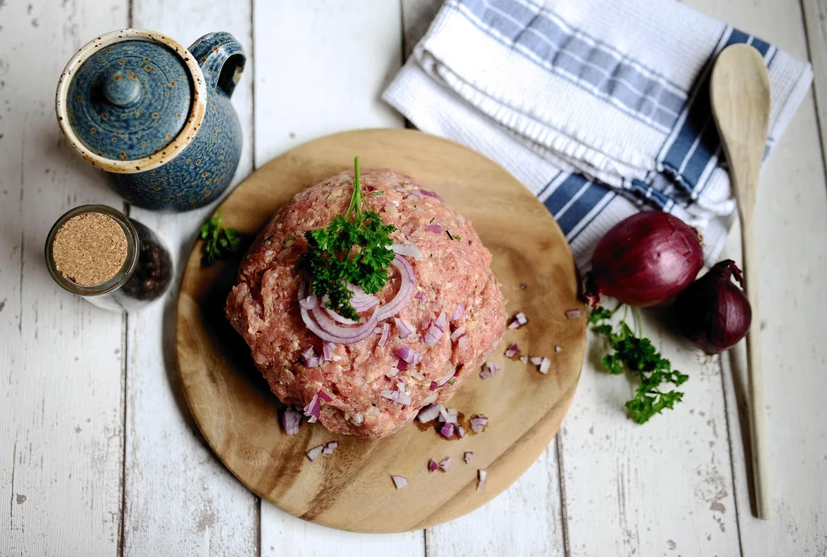 Raw ground beef on a wooden board with red onion, parsley and spices