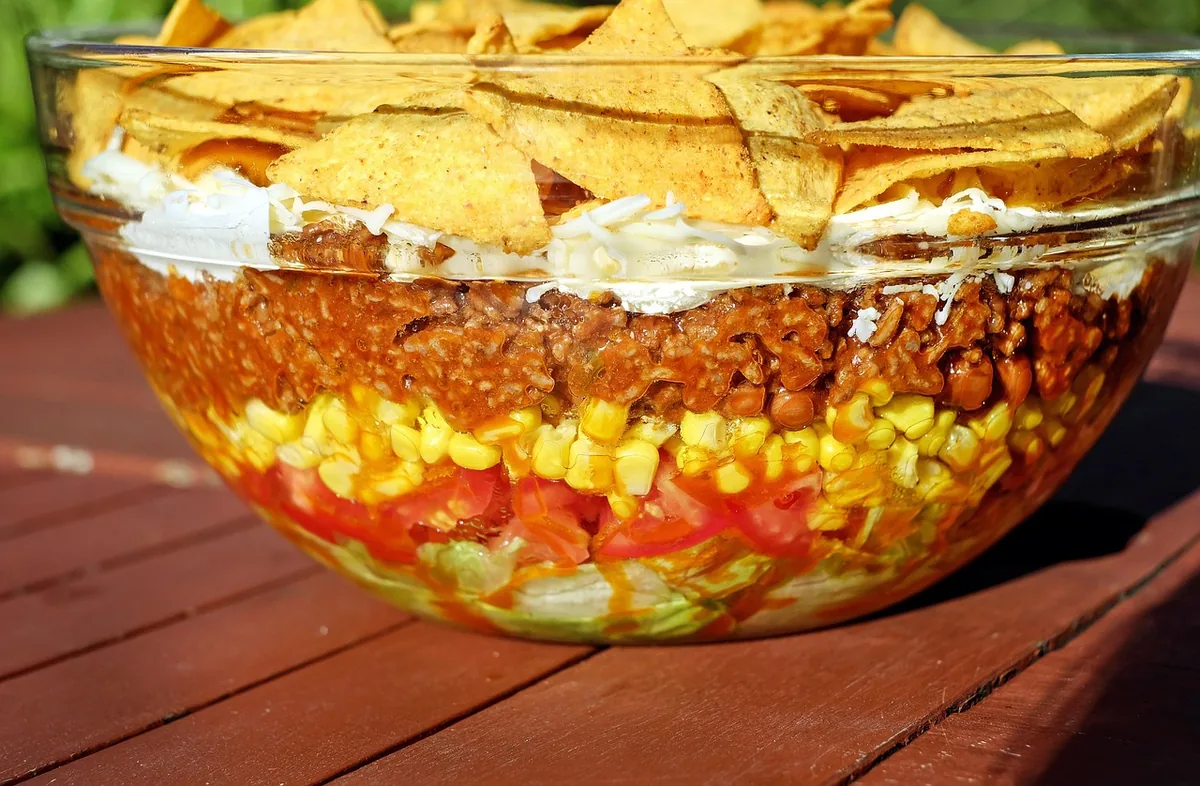 Layered taco salad with seasoned ground beef, corn, tomatoes and tortilla chips in a glass bowl