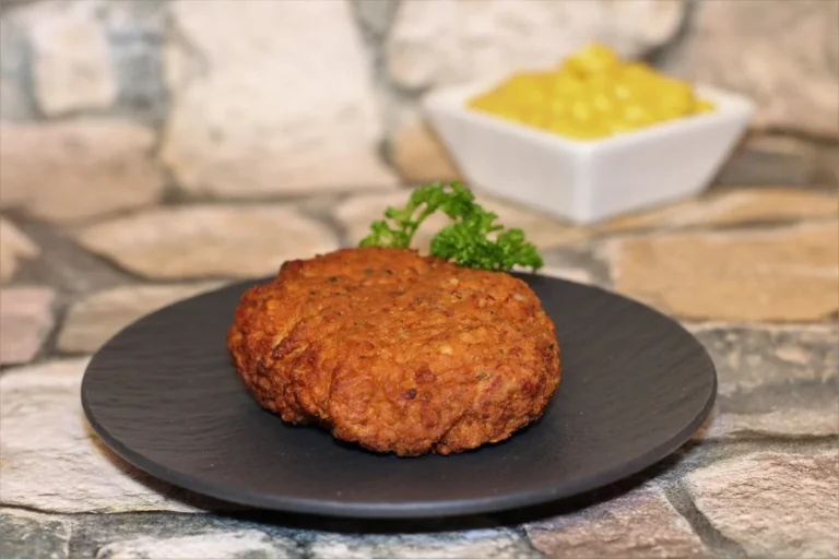 Golden pan-fried patty on a dark plate with a small bowl of mustard, the kind of crust to aim for with this salmon patty recipe