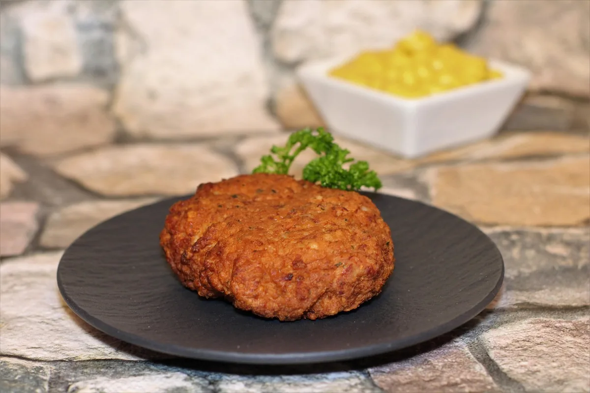 Golden pan-fried patty on a dark plate with a small bowl of mustard, the kind of crust to aim for with this salmon patty recipe