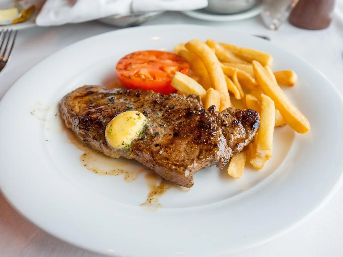 Seared steak topped with herb butter, served with fries and tomato