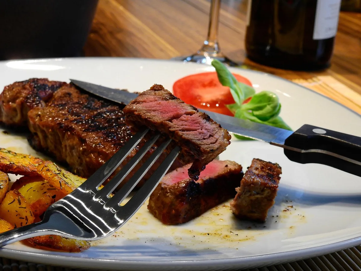 Steak cut open to show a pink center, served with roasted potatoes, like a reverse-seared chuck eye steak
