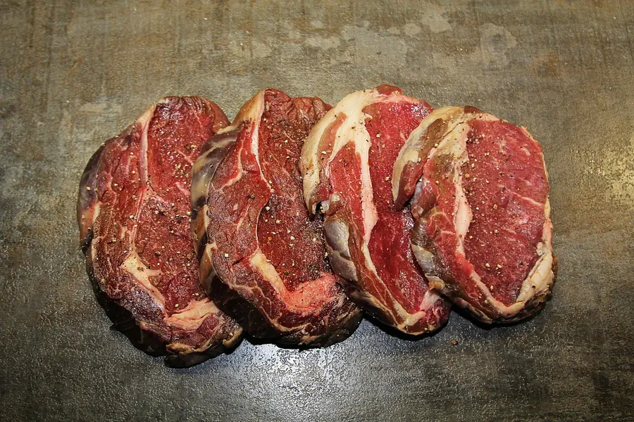 Four raw marbled boneless steaks seasoned with black pepper on a dark board