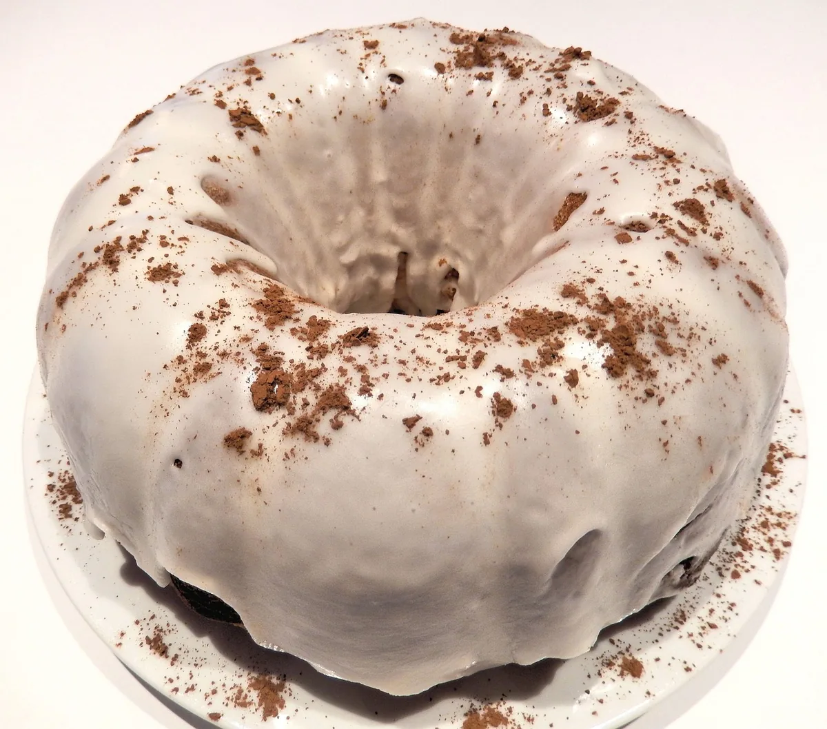 Bundt cake with a white glaze sprinkled with cocoa on a cake stand