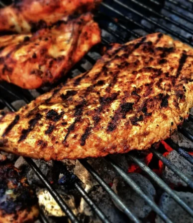 Seasoned smoked chicken breast with grill marks over hot coals