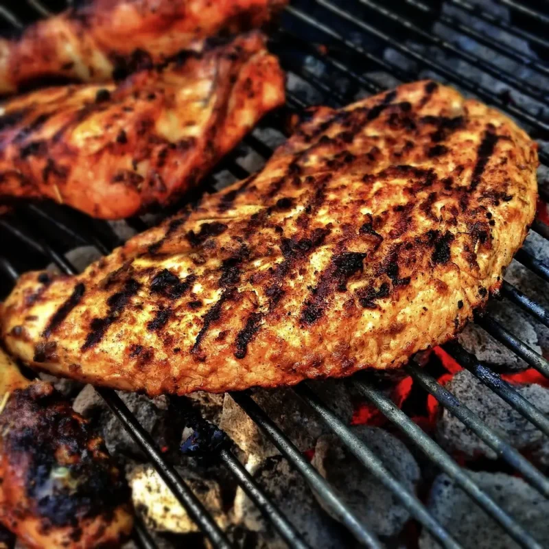 Seasoned smoked chicken breast with grill marks over hot coals