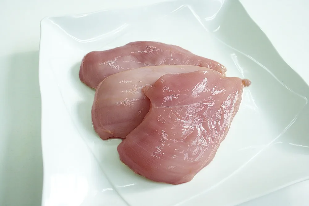 Raw boneless skinless chicken breasts on a white plate, ready for the brine