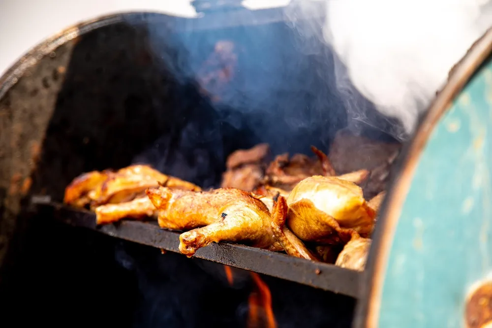 Chicken cooking on the rack of a barrel smoker over a wood fire