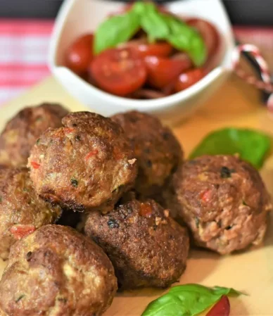 Oven baked meatballs on a board with basil and cherry tomatoes, showing how long to cook meatballs in oven